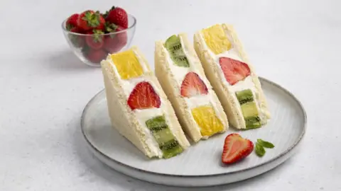 Japanese fruit sando hits high streets Dariia Chernenko/Getty Images Three sandwiches in white bread on a plate. Each sandwich contains cream, a strawberry, a piece of kiwi and a piece of pineapple. In the background is a small bowl of strawberries