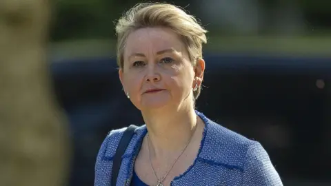 Government struggles to cut foreign aid spent on asylum hotels Getty Images Yvette Cooper walking along the pavement. She has blue eyes and is wearing a light blue jacket.