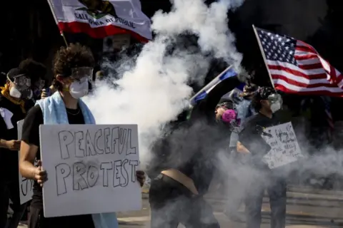 Mass protests against Trump across US as president holds huge military parade Getty Images A protester in LA throws a tear canister back towards police