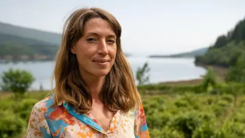 Fraudster jailed for selling fake 'Scottish-grown tea' Islay Henderson has shoulder length brown hair and smiles at the camera. She is wearing a floral top and is standing outdoors in front of a loch