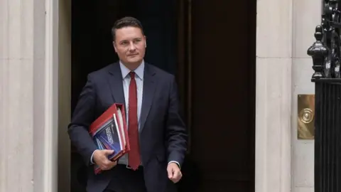 Hundreds of NHS quangos to be scrapped in 10-year health strategy PA Media Health Secretary Wes Streeting, wearing a dark suit and red tie, leaves 10 Downing Street holding a red folder
