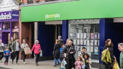 Government jobs support plans 'a mess', DWP officials tell BBC Getty Images People, including families, walking on a street past the Job Centre Plus employment office in Chester. The street is busy, the weather is dry but people are wearing coats.