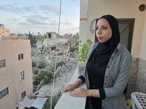 I feel like the life I had before the war was all made up BBC Hanya, who is wearing a black headscarf, looks out at a street filled with destroyed buildings, from her balcony
