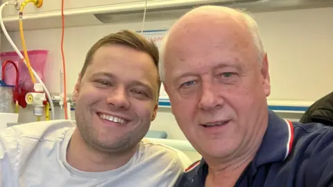 Dad gave me a kidney so I can have my dream wedding Brian Innes Kieran is smiling at the camera. He has short brown hair and is wearing a white t-shirt. Hi dad, Brian, is bald and is wearing a blue t-shirt.