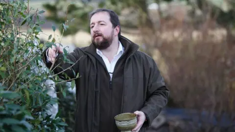 Fraudster jailed for selling fake 'Scottish-grown tea' Getty Images Thomas Robinson collects tea from a field. He is dressed in a white shirt, brown fleece and a brown wax jacket