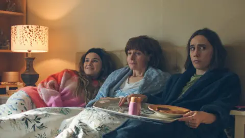 The dark comedy inspired by 'bleak' dating scene BBC/Various Artists Limited Left to right: In bed next to each other are Billie (Lizzie Davidson) wearing a pink jumper, Deb (Louise Brealey) wearing a white top and a blue dressing gown, and Josie (Kat Sadler) wearing a green top and a blue dressing gown and holding a tray with toast and a boiled egg on.