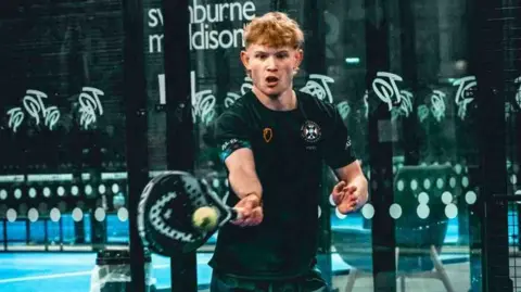 'I want to play the sport but I can't afford it' Daisy Whitlie A young man in sports kit strikes a ball with a padel racquet. He has an expression of intense concentration and looks to be exerting himself as the forehand swing connects.