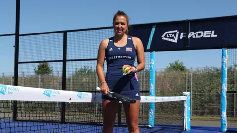 'I want to play the sport but I can't afford it' Getty Images A young woman dressed in a Great Britain team vest and skirt stands next to the net in the centre of an outdoor padel court on a cloudless, sunny day. She holds her racquet at waist level and a yellow ball in her other hand.