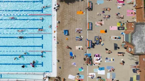 Health alerts come into force ahead of second heatwave EPA People sunbathe next to an outdoor lido in an aerial shot.