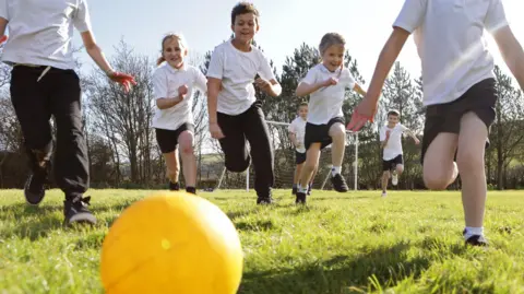 Ban 'no ball games' signs to get children off devices, play experts say Getty Images A group of children in black and white uniforms run towards a yellow ball on green grass.