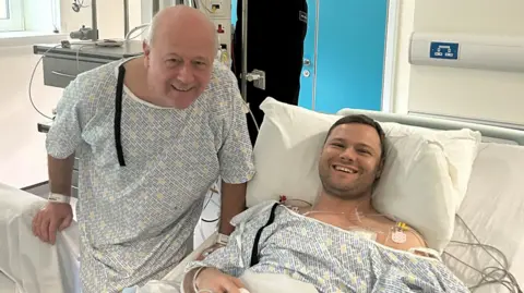 Dad gave me a kidney so I can have my dream wedding Kieran Innes Kieran is lying in a hospital bed and smiling. His dad Brian is standing beside the bed wearing a hospital gown. Brian is bald. Kieran has brown hair and a stubbly chin.