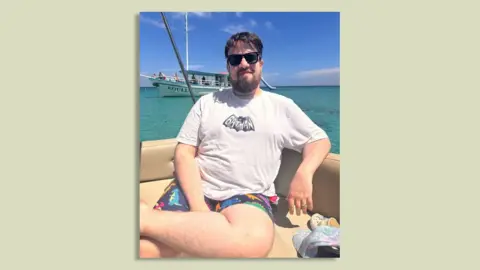 Wearing shorts still a 'grey area' as offices scrap dress codes Tony Hardy A man in a white Batman t-shirt with a picture of a bat on it and patterned dinosaur shorts sit on a boat at sea.