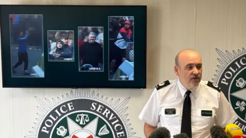 Police under attack in fifth night of unrest A constable is talking to the media. Behind him, on a screen are the images of four males.