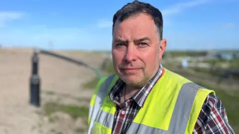 Truckloads of Scotland's rubbish will be exported to England, say experts David Balmer, with short dark hair and stubble, wears a checked shift and high visibility vest. He's standing in front of a methane extraction pipe on an active landfill site.