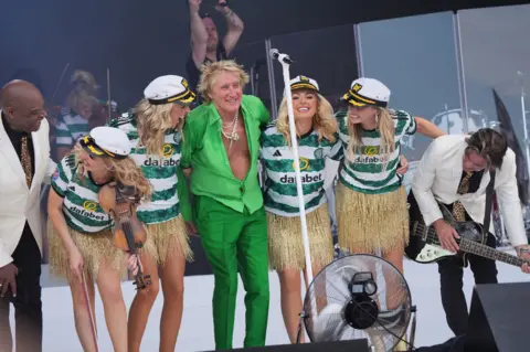 Old school charm from another era EPA Rod Stewart and his band - he is wearing a bright green suit, while his band have gold skirts, Celtic football shirts and sailors' caps on