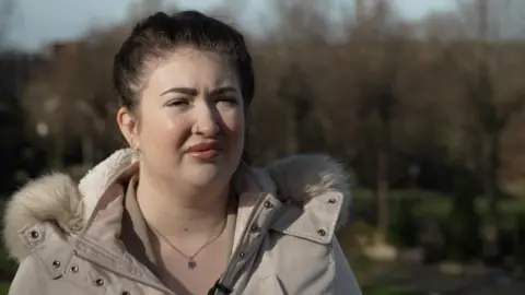 Is surveillance culture fuelling child cyberstalking? A young woman with dark hair wears a beige winter coat in a park.
