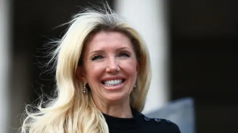 Our sister died because of our mum's cancer conspiracy theories, say brothers Getty Images Kate Shemirani, pictured in close-up with a long lens at an anti-vaccine protest in 2020. She wears a black dress with buttons at the shoulder and has long blonde hair that hangs in loose curls over her right shoulder. She is smiling brightly.