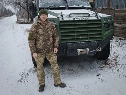 A Russian soldier takes the stand for an execution Handout Vitalii Hodniuk stands in uniform in front of a military truck on a snowy street.