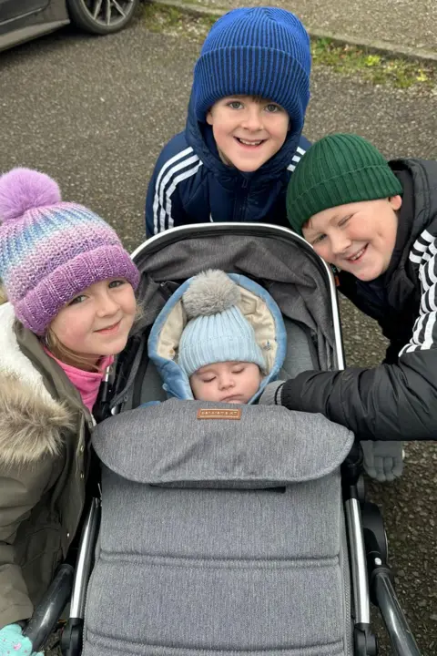 Parents' worldwide search for babies with son's rare condition Family photo Jack is in a pushchair surrounded by his two older brothers and older sister. All are wearing bobble hats and smiling. Jack is sleeping.