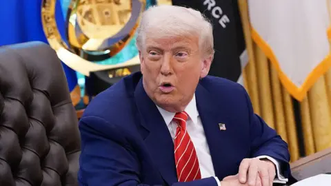 What we know about Trump's latest travel ban Getty Images US President Donald Trump sits at a desk in the Oval Office of the White House. He is wearing a blue suit with an American flag pinned to the lapel.