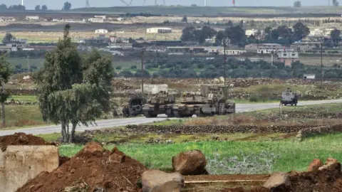 BBC team detained by Israeli forces in southern Syria AFP File photo showing Israeli tanks and a military bulldozer driving through the Abu Diab military post, on the southern outskirts of the Syrian city of Quneitra (19 March 2025)