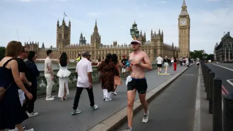 Heatwave eases as rainy weather blows in across parts of UK Reuters A man jogs across Westminster Bridge towards the camera with other people walking across in the opposite direction. The Houses of Parliament can be seen in the background.
