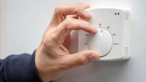 NI pensioners could have payments restored Getty Images A mans hand adjusts a white thermostat on a white wall. The mans arm is covered by a navy sweatshirt.