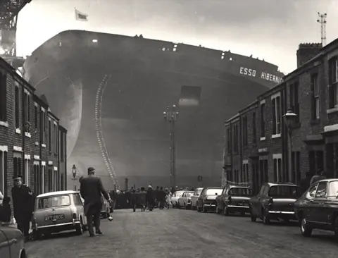 Governments have neglected the North East for decades Newcastle City Council Photo of huge ship, Esso Hibernia at the end of street showing houses, cars and people