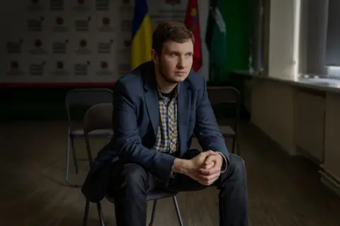 A Russian soldier takes the stand for an execution Local prosecutor Mykyta Manevskyi, who is wearing jeans, a blue suit jacket and yellow checked shirt, sits on a chair in a media room in the district prosecutor's office.