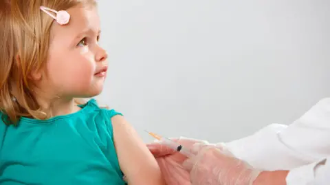 Parents face barriers to vaccinating children, says report Getty Images A young child wearing a green top has her sleeve rolled up and is ready to get a vaccine from a doctor (unpictured) whose arms and hands are in view, who is holding a vaccine