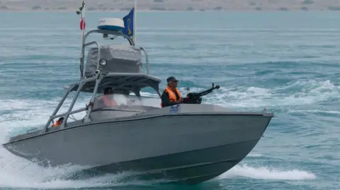 What is the Strait of Hormuz and why does it matter? Getty Images A boat patrols the waters off an arid coast, with a man in a bright orange jacket onboard holding a machine gun
