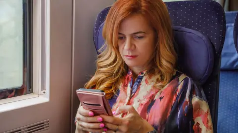 No phone signal on your train? There may be a fix Getty Images Woman sitting on train looking at her phone