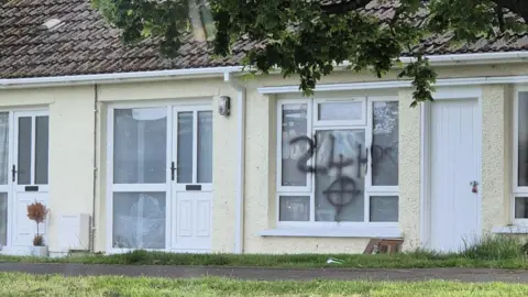 Police under attack in fifth night of unrest Graffiti in black spray paint has been daubed across a house. The markings show a cross in a circle and 24 hours.