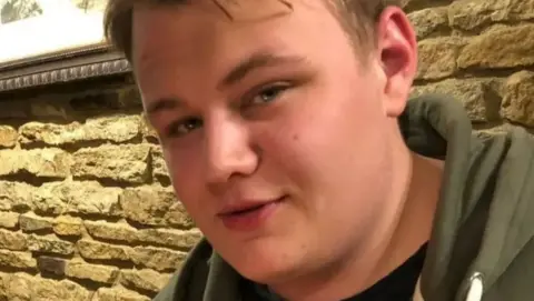 Harry Dunn police 'could and should have arrested' diplomat Dunn family Close up of a young man's face. He is looking directly at the camera and is wearing a green hooded top.