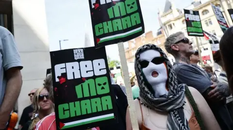 Rapper released on unconditional bail over terror charge TOLGA AKMEN/EPA-EFE/Shutterstock A person wearing a white balaclava and a headscarf holds a poster that says 'Free Mo Chara' . Other people in the background also hold placards