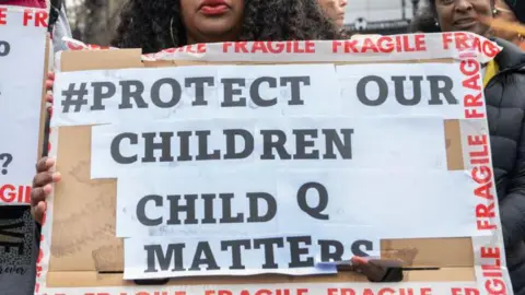 Child Q strip-search was gross misconduct, panel finds Getty Images A protester holds a cardboard sign reading “#Protect our children, Child Q matters,” bordered with red “fragile” tape.