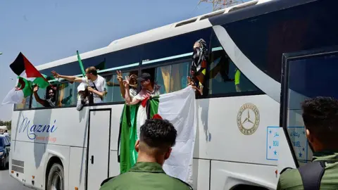 Six Gaza aid boat activists deported from Israel Getty Images Activists lean out of the side of a bus waving Palestinian and Algerian flags.