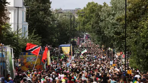 Future of Notting Hill Carnival 'in jeopardy' Reuters A large crowd fills a tree-lined street during Notting Hill Carnival, with colourful floats, flags - including the Trinidad and Tobago flag - and banners visible among the dense procession.