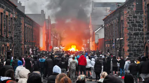Disorder after alleged sex assault 'unwarranted', says Jim Allister Pacemaker A large crowd standing on the street in Ballymena. There are buildings on either side and a fire in the distance. Smoke is rising into the sky.