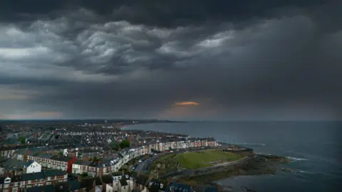 Heatwave eases as rainy weather blows in across parts of UK PA Media A landscape image of Whitley Bay in North Tyneside along the coastline. Dark clouds have gathered across the sky.