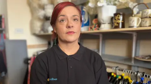 Government jobs support plans 'a mess', DWP officials tell BBC Kerry Ritson is wearing a black polo shirt with the GoodLives logo on. She has her hair dyed dark red. She's sitting in the charity shop which she works.