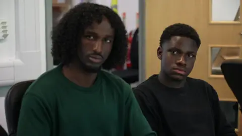 'Child Q case made me fear could this happen to me' BBC Adnan, 18, wears a dark green top and is sitting at a table inside an office room beside Edem, 18, in a black top, both listening to the discussion