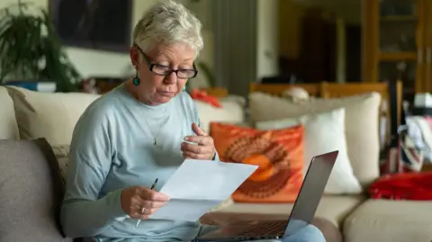 Reactions to winter fuel payment U-turn Getty Images An elderly lady looks at a bill while sitting with a laptop on her knee on a sofa