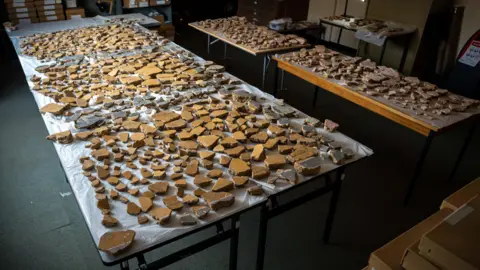 Huge archaeological puzzle reveals Roman London frescoes Tony Jolliffe/BBC News Hundreds of fragments of plaster laid out on several tables. Mainly yellow pieces making up three square panels with darker columns in between.
