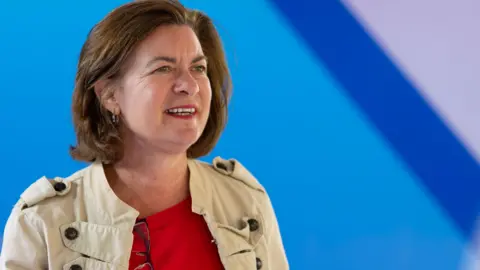 'The Heads of the Valleys road swallowed part of my garden' Getty Images Eluned Morgan looks into the distance. She is wearing a red top and a fawn military style jacket. Behind her is a blurred blue background.