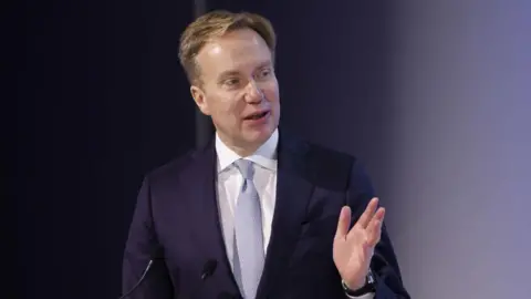 Turmoil and trade wars dominate 'summer Davos' Getty Images Borge Brende, president of the World Economic Forum, speaks in front of two small microphones, wearing a navy blue suit