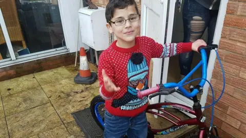 Child abuse training failures before Alfie Steele's Droitwich murder Family handout A boy stands on a garden patio with a bike. He has dark brown hair and glasses, and he is wearing a red Christmas jumper with a penguin on it. The bike is dark red with blue handlebars.