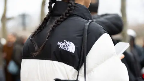 North Face and Cartier hit by cyber attacks Getty Images The back of a young woman wearing a black and white puffer jacket the The North Face logo on it.
