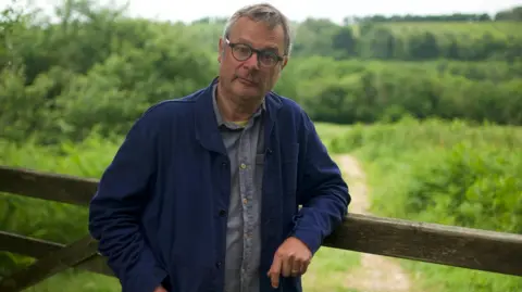 Warning over 'dirty secret' of toxic chemicals on farmers fields BBC/Kevin Church Hugh Fearnley-Whittingstall is leaning on a fence with green countryside behind him.