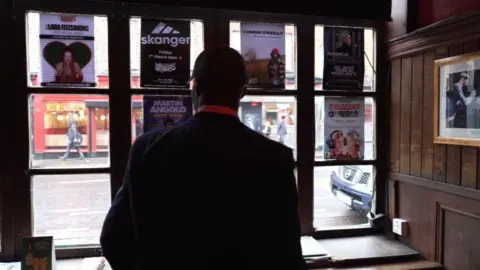 Ticket touts employing workers to bulk-buy for concerts A picture of the back of a man's head, who is wearing a black baseball cap. In front of him is a window with flyers in it